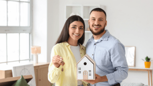A man and woman standing in new clean house. Woman is holding keys, man is holding a house model.
